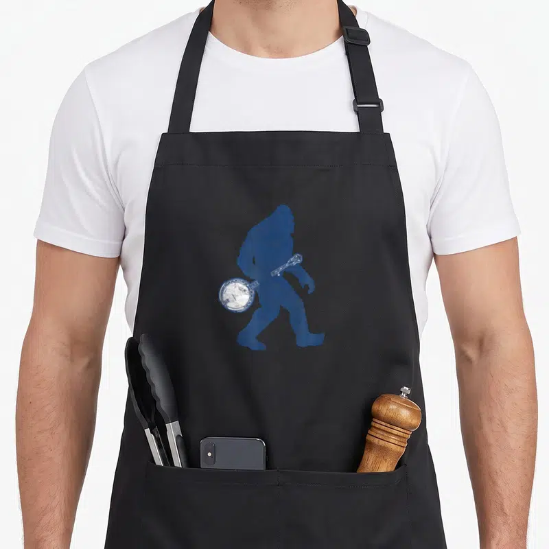 Banjo bigfoot apron - Blue distressed silhouette of walking Bigfoot holding a banjo — shown on a black cotton canvas apron against a white background