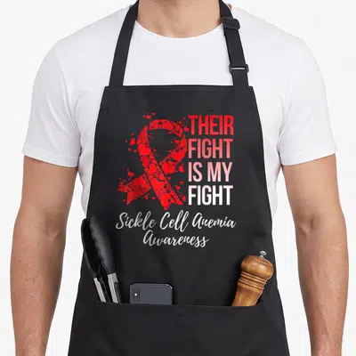 Their sickle cell awareness apron - Red heart-shaped awareness ribbon next to gradient text reading Their Fight Is My — shown on a black cotton canvas apron against a white background