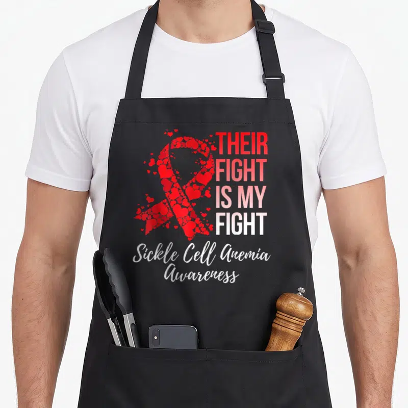 Their sickle cell awareness apron - Red heart-shaped awareness ribbon next to gradient text reading Their Fight Is My — shown on a black cotton canvas apron against a white background