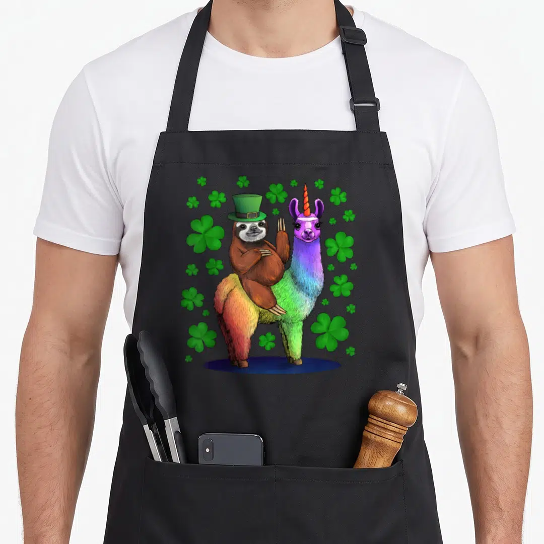 Sloth st patrick day aprons - Cartoon brown sloth in green hat riding rainbow llama unicorn with scattered green — shown on a black cotton canvas apron against a white background