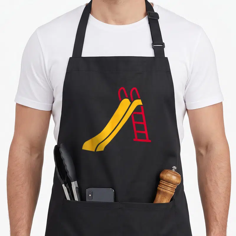 Slide playground apron - Yellow slide connected to a red ladder in minimalist flat style — shown on a black cotton canvas apron against a white background