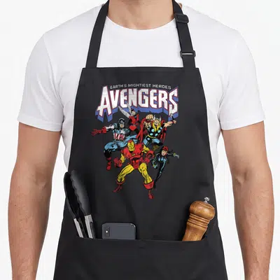 Vintage shot novelty apron - EARTH'S MIGHTIEST HEROES AVENGERS text above five superheroes in red blue yellow and white — shown on a black cotton canvas apron against a white background
