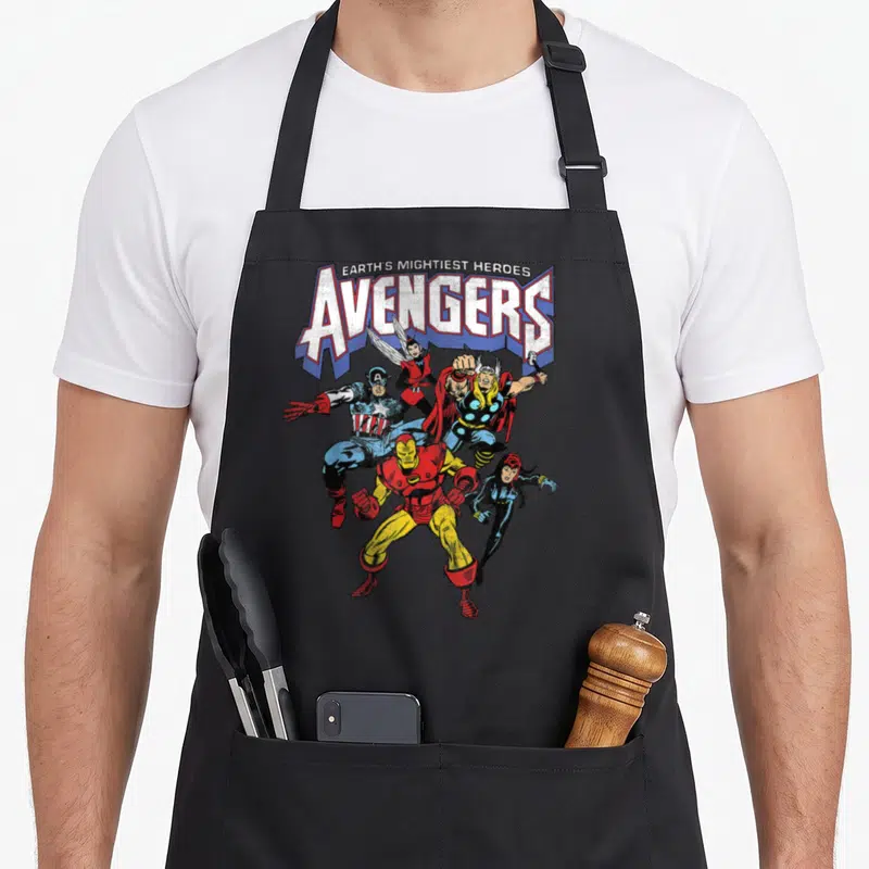 Vintage shot novelty apron - EARTH'S MIGHTIEST HEROES AVENGERS text above five superheroes in red blue yellow and white — shown on a black cotton canvas apron against a white background