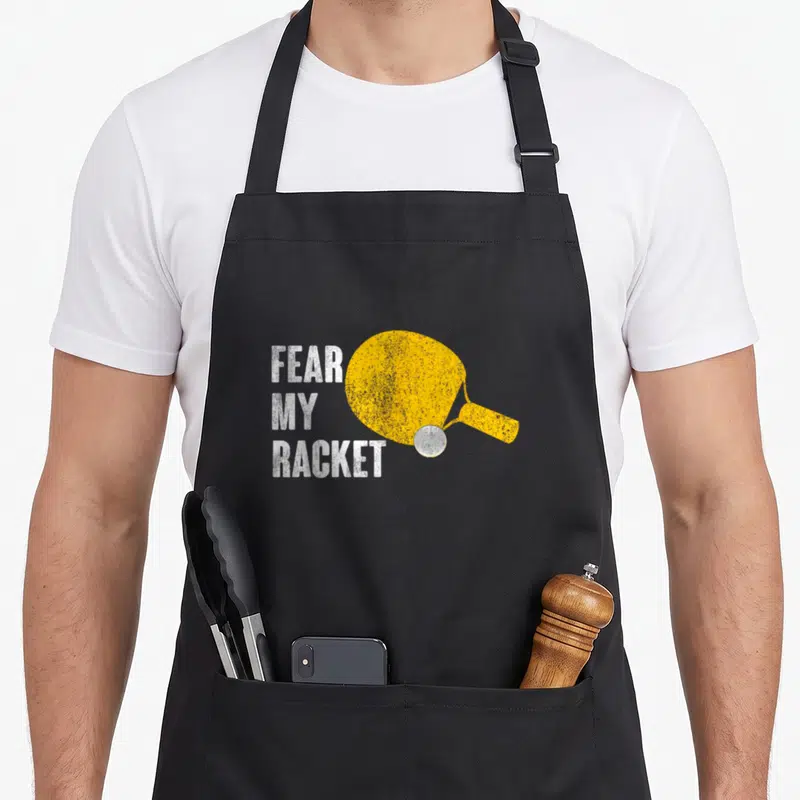 Fear table apron - Yellow paddle graphic with stacked white text reading Fear My Racket and a silver ball — shown on a black cotton canvas apron against a white background