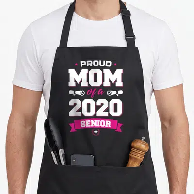 Proud class senior apron - Stacked text proud mom 2020 senior with pink ribbon and graduation cap icon — shown on a black cotton canvas apron against a white background