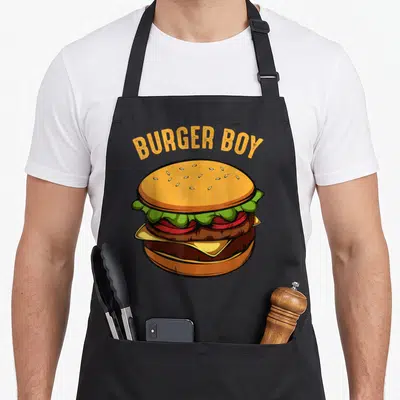 Hamburger food aprons - Cartoon double cheeseburger with arched BURGER BOY text in orange and yellow — shown on a black cotton canvas apron against a white background