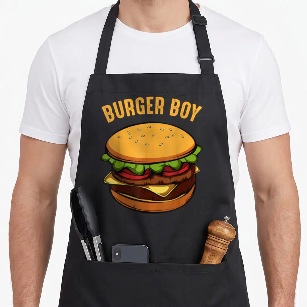 Hamburger food aprons - Cartoon double cheeseburger with arched BURGER BOY text in orange and yellow — shown on a black cotton canvas apron against a white background