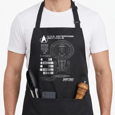 Generation star apron - White line-art blueprint of the U.S.S. Enterprise NCC-1701-D with technical data — shown on a black cotton canvas apron against a white background