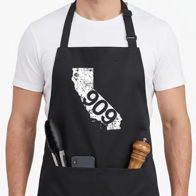 San triple g mavs apron - Distressed white California map with diagonal grey 909 text — shown on a black cotton canvas apron against a white background