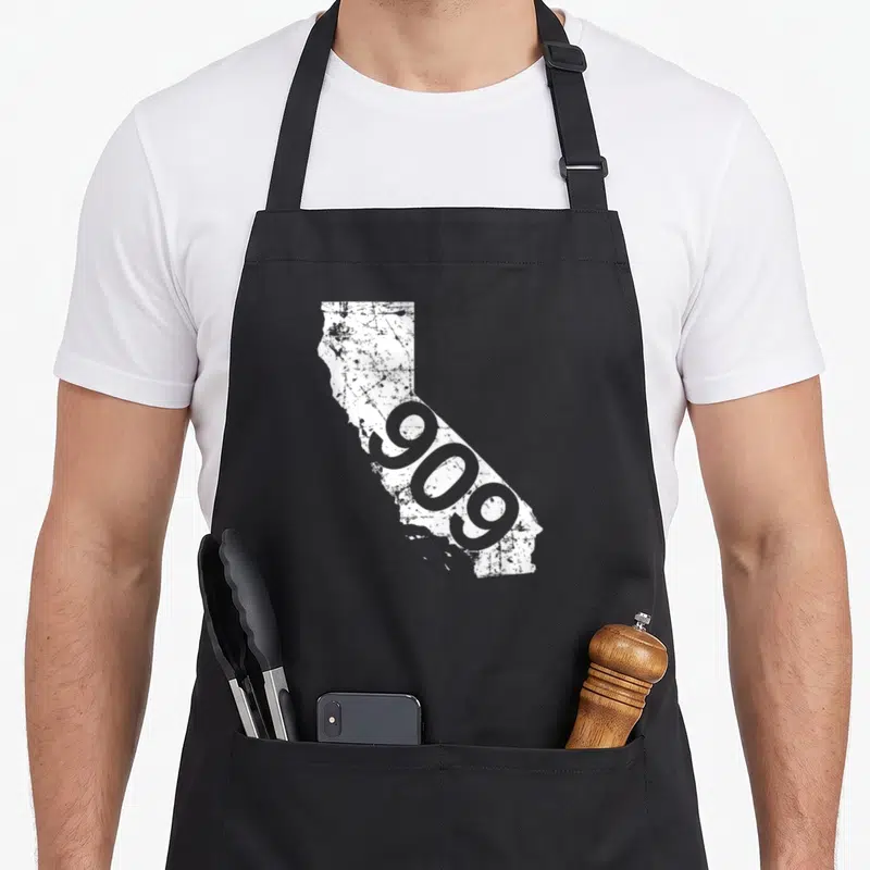 San triple g mavs apron - Distressed white California map with diagonal grey 909 text — shown on a black cotton canvas apron against a white background