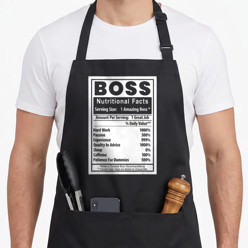 Bosss employee aprons - Nutrition label graphic listing boss traits like hard work 1000% and sleep 0% in black and white — shown on a black cotton canvas apron against a white background
