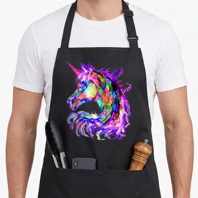 Unicorn kawaii apron - Multicolored unicorn head facing left in purple blue pink yellow green cartoon art — shown on a black cotton canvas apron against a white background