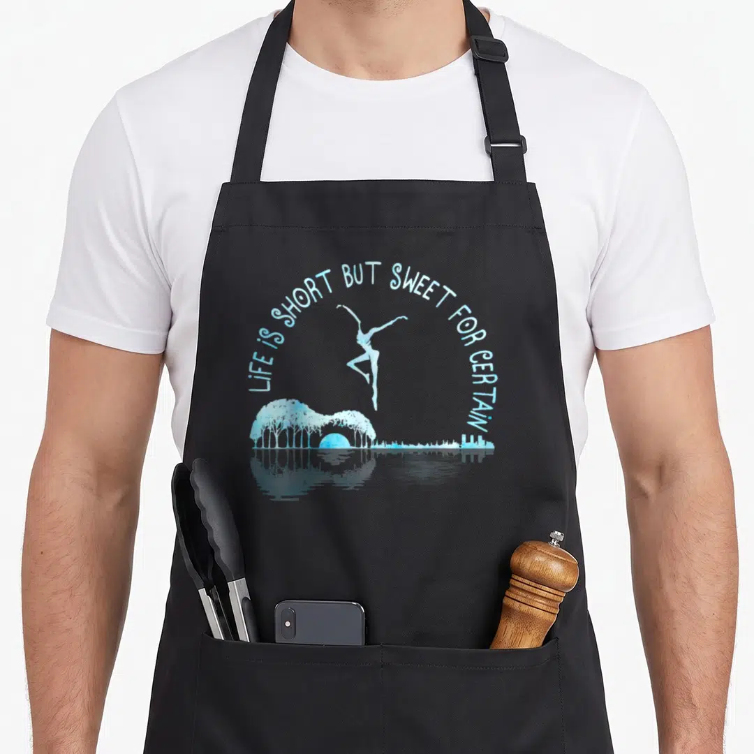 But music lovers apron - Ballerina leaping above guitar-shaped hill with trees and sun, text LIFE IS SHORT BUT SWEET — shown on a black cotton canvas apron against a white background