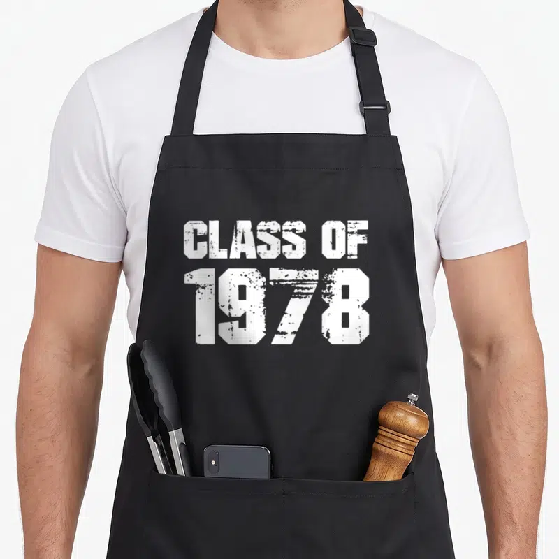 Reunion graduation apron - White distressed text reading CLASS OF 1978 stacked vertically on black fabric — shown on a black cotton canvas apron against a white background