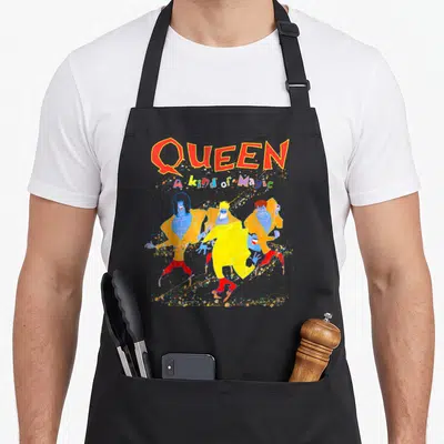 Kind magic apron - Four blue figures in yellow jackets and red pants dancing under QUEEN text with confetti — shown on a black cotton canvas apron against a white background