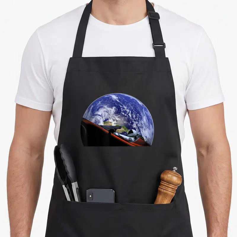 Starman space city company apron - Photo of Earth and astronaut in red spacecraft floating in space — shown on a black cotton canvas apron against a white background