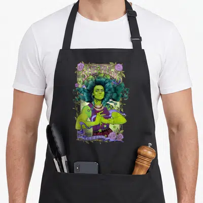 She floral apron - Green She-Hulk in purple rose frame with arched text and ribbon banner reading SHE WILL NOT BE — shown on a black cotton canvas apron against a white background