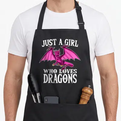Funny costume dragon apron - Pink and purple cartoon dragon surrounded by white text Just A Girl Who Loves Dragons — shown on a black cotton canvas apron against a white background