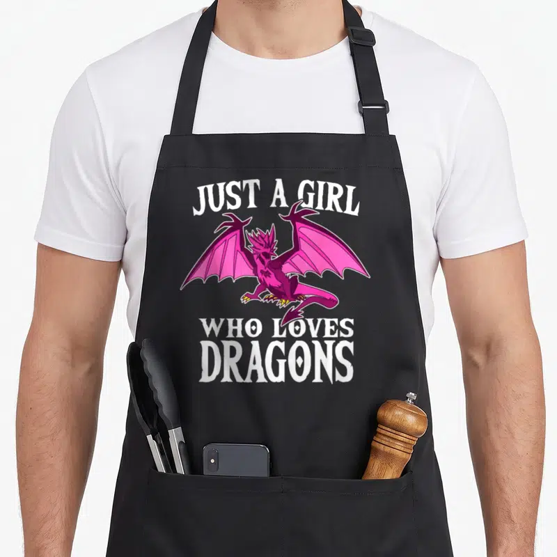 Funny costume dragon apron - Pink and purple cartoon dragon surrounded by white text Just A Girl Who Loves Dragons — shown on a black cotton canvas apron against a white background