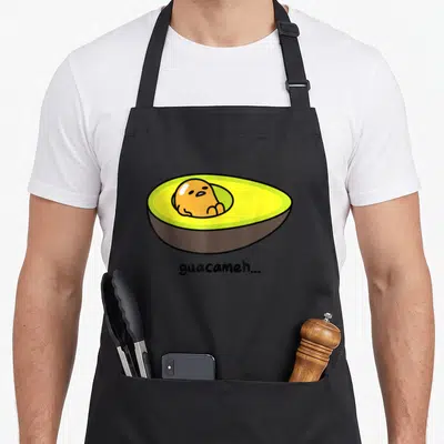 Gudetama avocado apron - Orange character inside halved avocado with guacameh text below — shown on a black cotton canvas apron against a white background