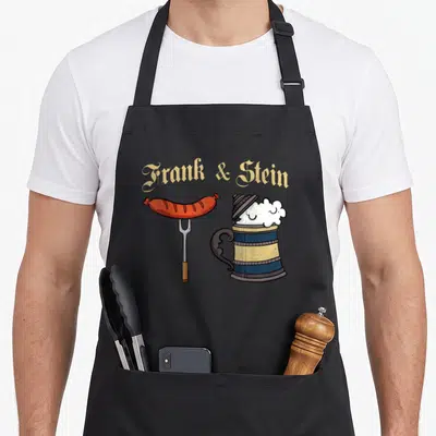 Frank german oktoberfest aprons - Cartoon sausage on fork and blue beer stein with Frank & Stein text in gold — shown on a black cotton canvas apron against a white background