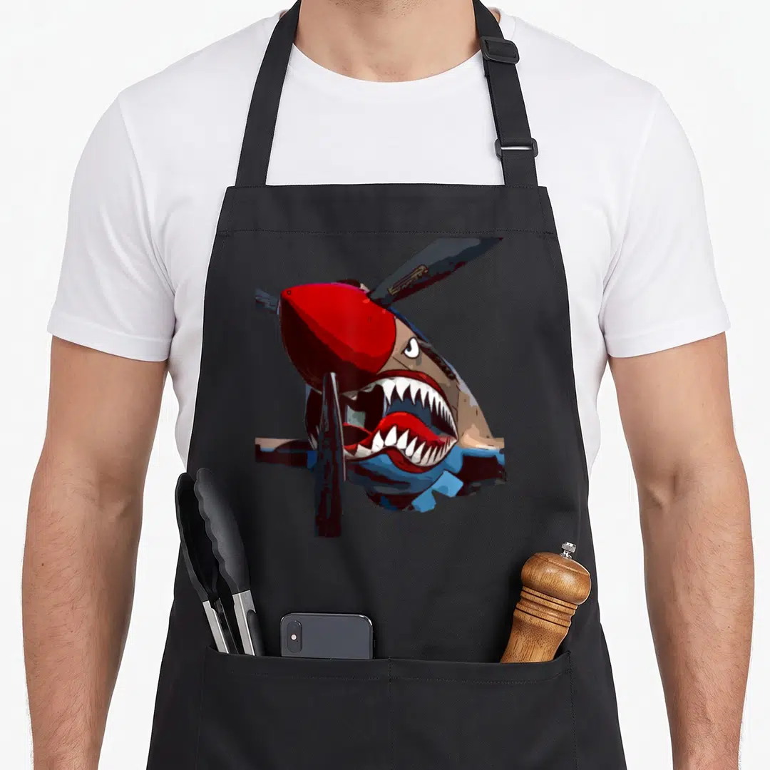 Warhawk aircraft apron - Realistic shark nose art on fighter plane fuselage with red cowling and propeller blades — shown on a black cotton canvas apron against a white background