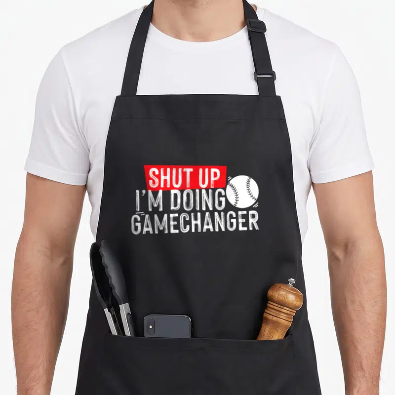Shut baseball apron - White text SHUT UP in red box next to baseball illustration — shown on a black cotton canvas apron against a white background