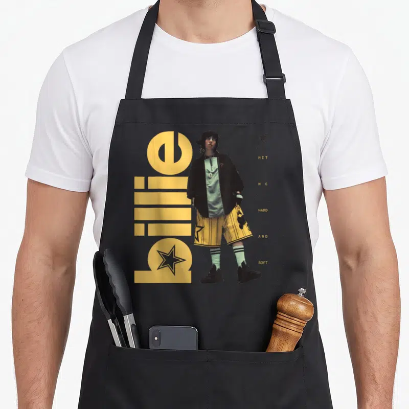 Hit hard apron - Billie Eilish photo with yellow billie text and HIT ME HARD AND SOFT words — shown on a black cotton canvas apron against a white background