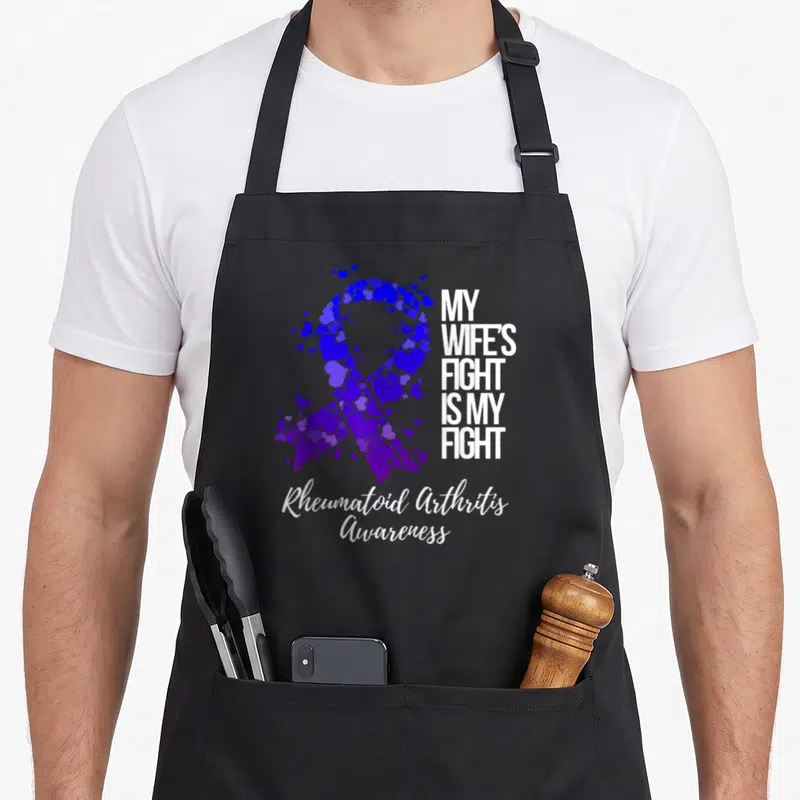 Rheumatoid wife apron - Purple heart ribbon graphic with My Wife's Fight Is My Fight text and script awareness label — shown on a black cotton canvas apron against a white background