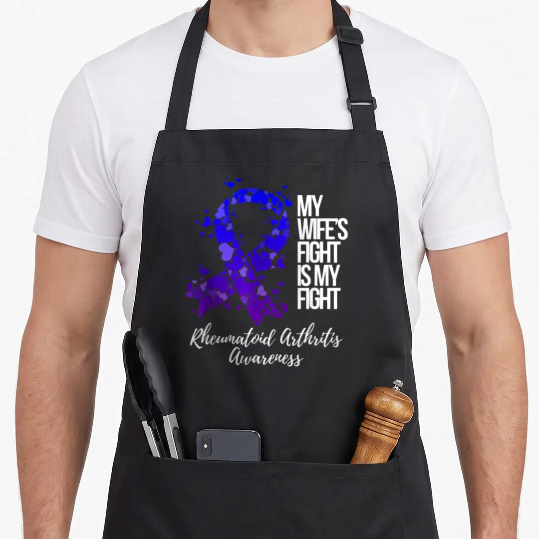 Rheumatoid wife apron - Purple heart ribbon graphic with My Wife's Fight Is My Fight text and script awareness label — shown on a black cotton canvas apron against a white background