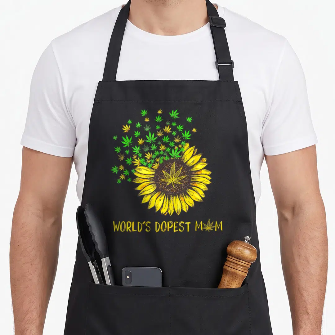 Weed sunflower apron - Yellow sunflower with green cannabis leaf center and WORLD'S DOPEST MOM text below — shown on a black cotton canvas apron against a white background