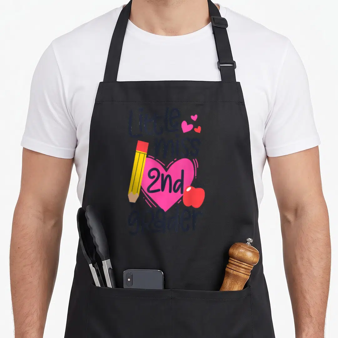 Miss 2nd apron - Little miss 2nd grader text with pink heart, yellow pencil, and red apple — shown on a black cotton canvas apron against a white background