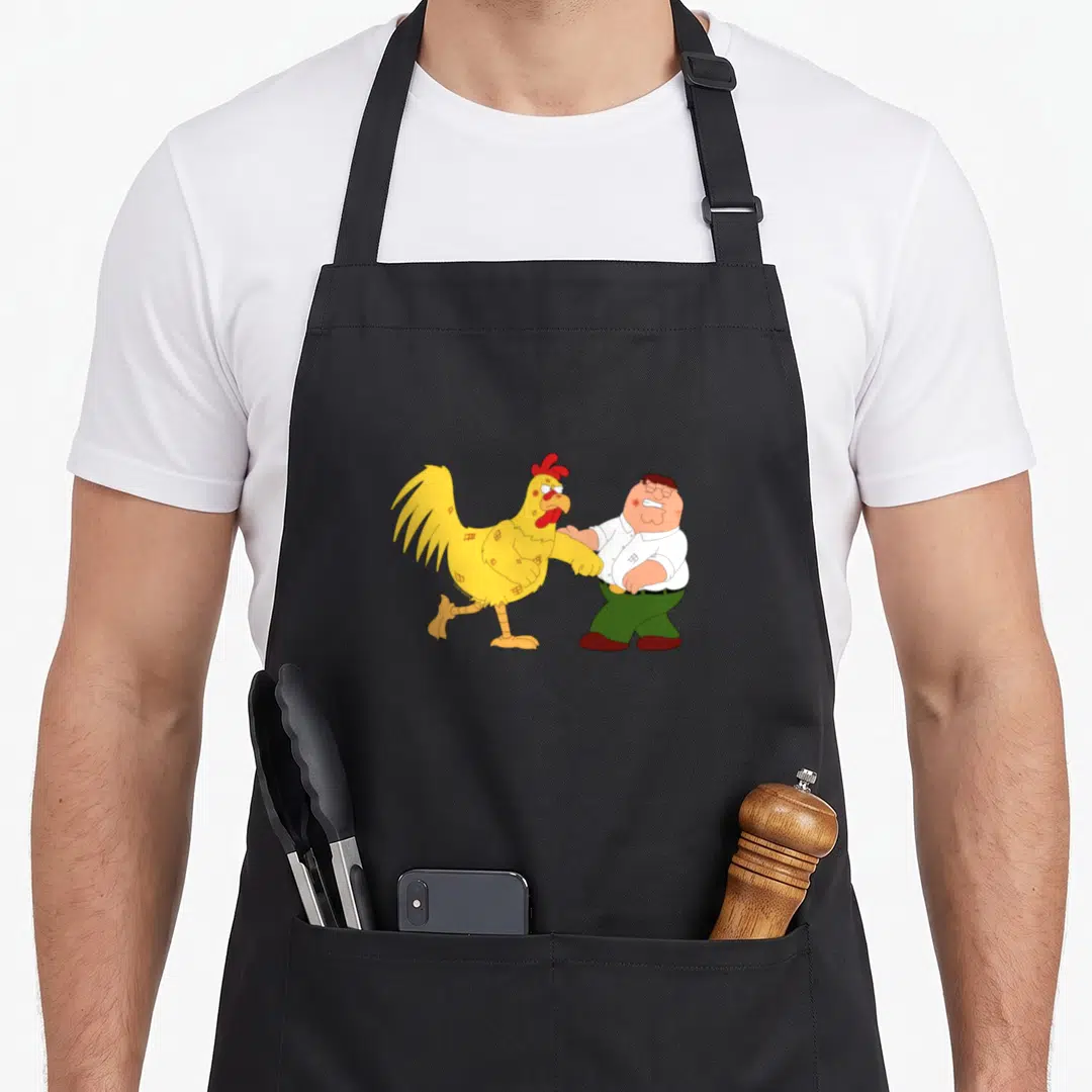 Fighting chicken apron - Cartoon yellow chicken and man in white shirt facing each other in a fight pose — shown on a black cotton canvas apron against a white background