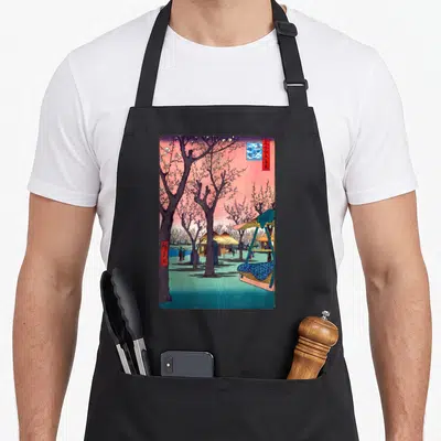 Traditional cherry print apron - Japanese woodblock print of cherry trees, huts, and red blue text boxes on pink — shown on a black cotton canvas apron against a white background