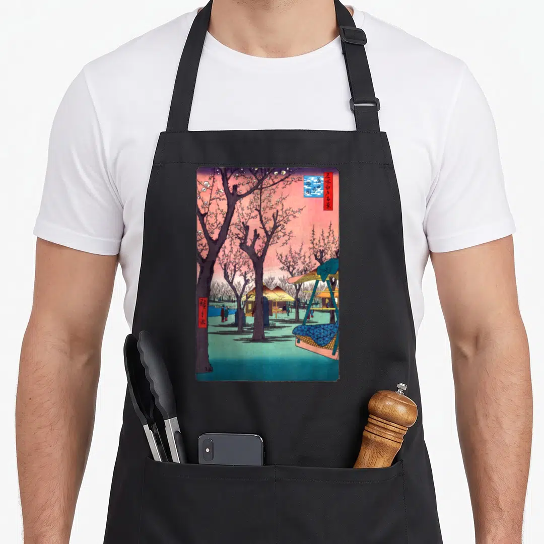 Traditional cherry print apron - Japanese woodblock print of cherry trees, huts, and red blue text boxes on pink — shown on a black cotton canvas apron against a white background