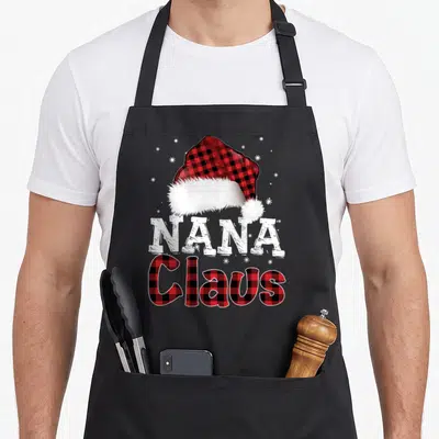 Costume santa aprons - Nana Claus text under red black plaid Santa hat with white snowflakes — shown on a black cotton canvas apron against a white background