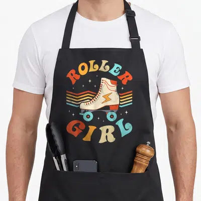 Skater 70s apron - Retro roller skate with ROLLER GIRL text in orange yellow beige and light blue — shown on a black cotton canvas apron against a white background