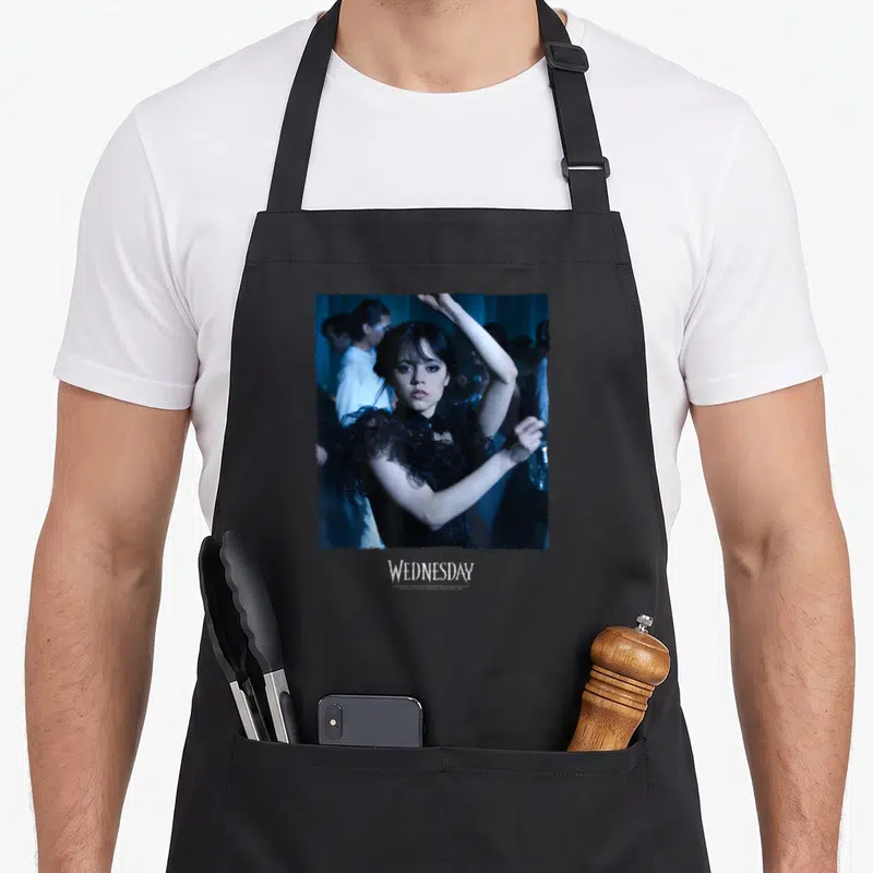 Wednesday queen apron - Square photo of Wednesday Addams dancing in blue tones with WEDNESDAY text below — shown on a black cotton canvas apron against a white background