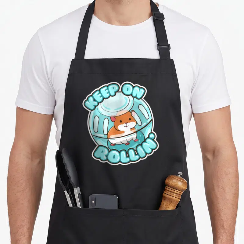Rolling pet apron - Cartoon hamster in blue wheel with arched text KEEP ON ROLLIN white border — shown on a black cotton canvas apron against a white background