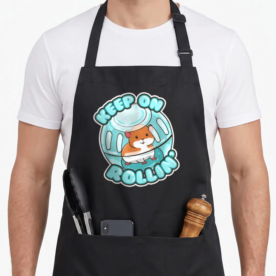 Rolling pet apron - Cartoon hamster in blue wheel with arched text KEEP ON ROLLIN white border — shown on a black cotton canvas apron against a white background