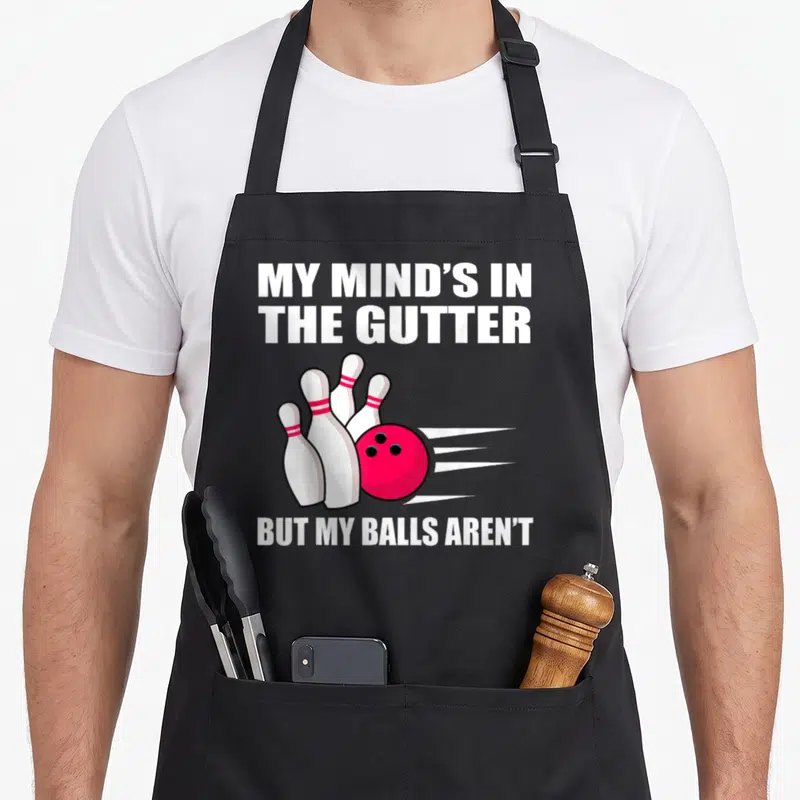 Bowling split lover apron - Red bowling ball hitting white pins with My Mind's In The Gutter text — shown on a black cotton canvas apron against a white background