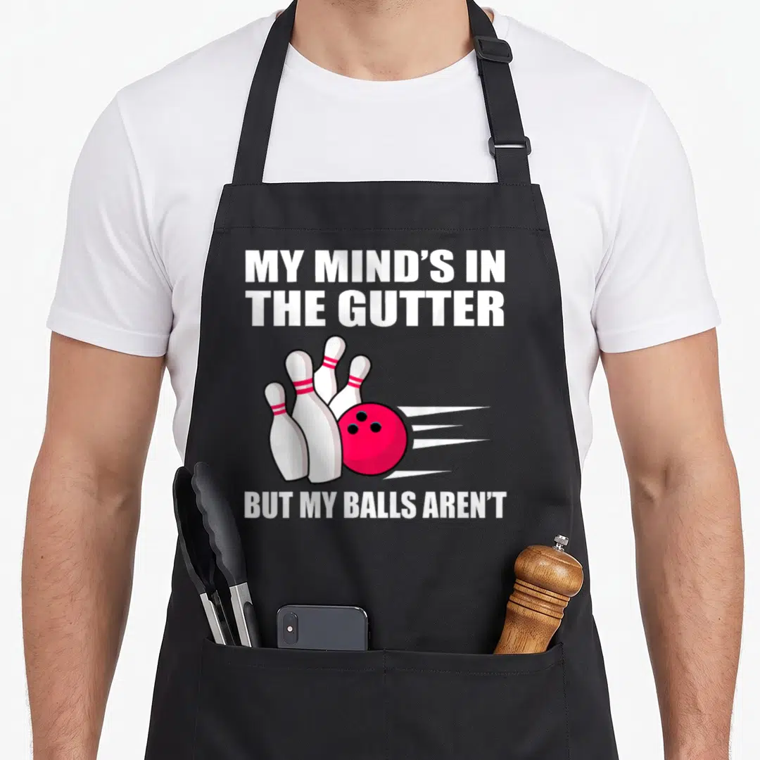 Bowling split lover apron - Red bowling ball hitting white pins with My Mind's In The Gutter text — shown on a black cotton canvas apron against a white background