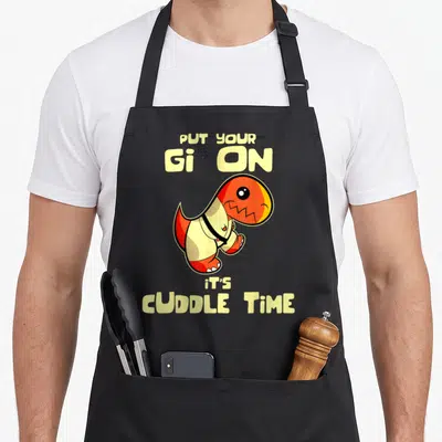 Bjjj brazilian jiu jitsu apron - Orange dinosaur wearing gi with text PUT YOUR Gi ON it'S CUDDLE TIME — shown on a black cotton canvas apron against a white background