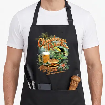 Paradise cheeseburgers apron - Tropical cheeseburger, toucan, beer mug, and Heaven on Earth text in orange and green — shown on a black cotton canvas apron against a white background