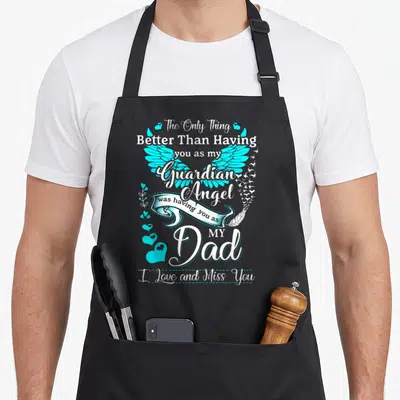 Missing angels and aprons - Cyan angel wings with white ribbon and text reading Better Than Having you as my Guardian — shown on a black cotton canvas apron against a white background