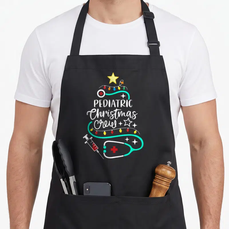 Pediatric christmas apron - Teal stethoscope and syringe forming a Christmas tree shape with stacked white text — shown on a black cotton canvas apron against a white background