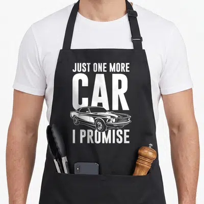 Cute promise car apron - White text Just One More Car I Promise with line art muscle car — shown on a black cotton canvas apron against a white background