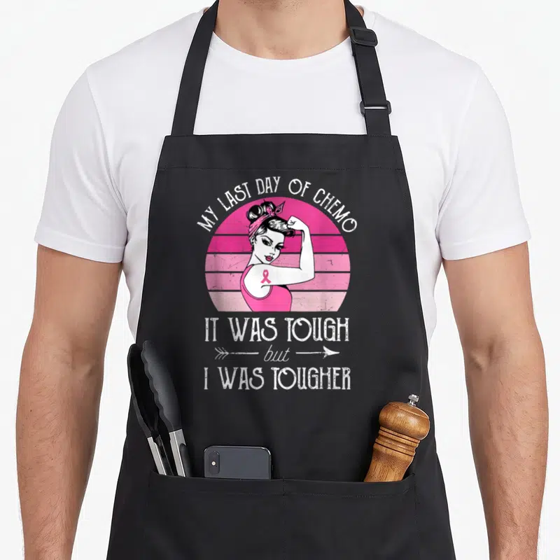 Mein tag apron - Retro woman flexing arm pink striped sun MY LAST DAY OF CHEMO text pink ribbon — shown on a black cotton canvas apron against a white background