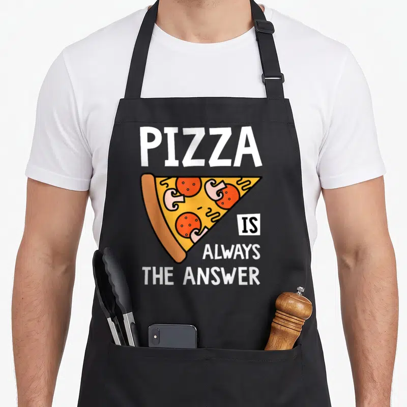 Answer pizza apron - Cartoon pizza slice with text PIZZA IS ALWAYS THE ANSWER in white orange yellow red — shown on a black cotton canvas apron against a white background