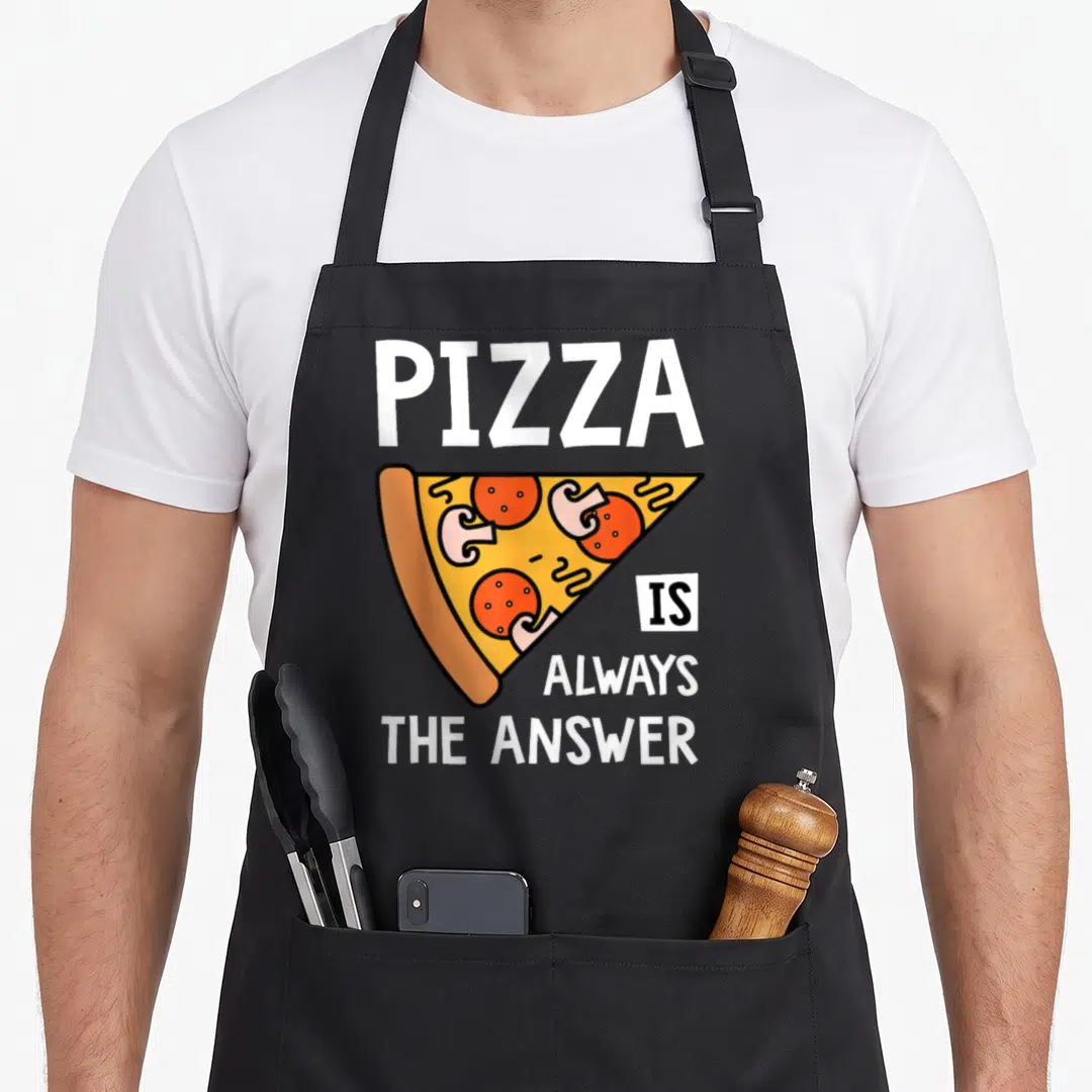 Answer pizza apron - Cartoon pizza slice with text PIZZA IS ALWAYS THE ANSWER in white orange yellow red — shown on a black cotton canvas apron against a white background